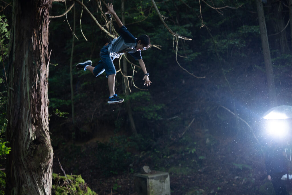 Teenage boy falling in mid air in dark Japanese forest