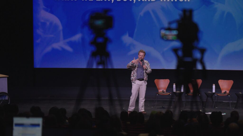 A speaker on stage and cameras filming